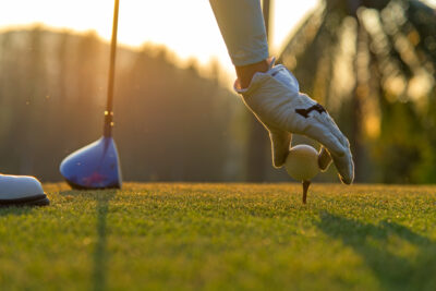 Hand asian woman putting golf ball on tee with club in golf course on evening and sunset time a for healthy sport.  Lifestyle Concept