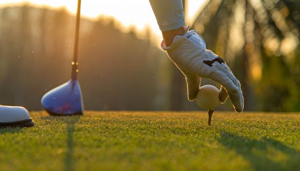 Hand asian woman putting golf ball on tee with club in golf course on evening and sunset time a for healthy sport.  Lifestyle Concept